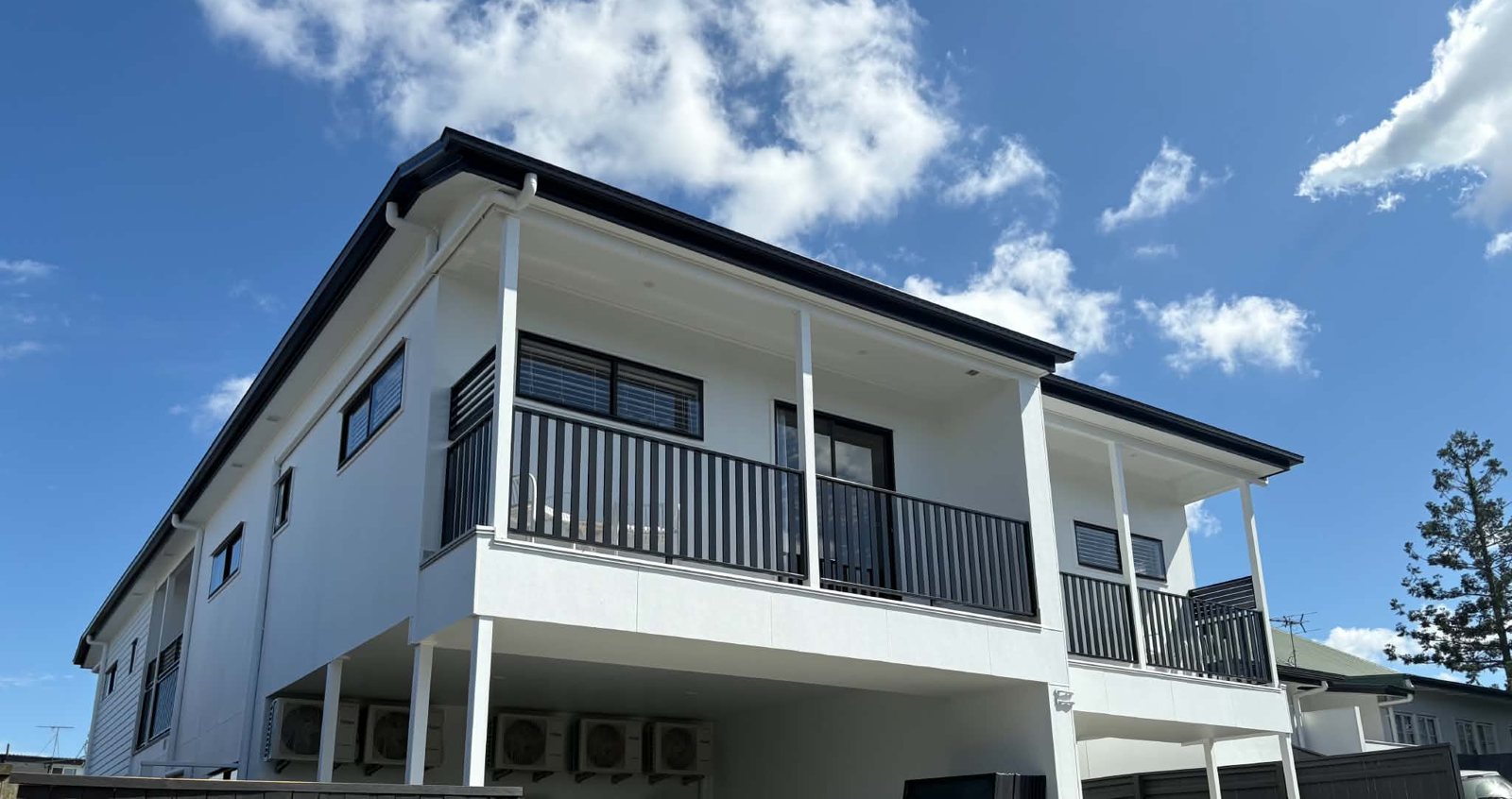 Finished duplex with white render, black balustrades and covered parking