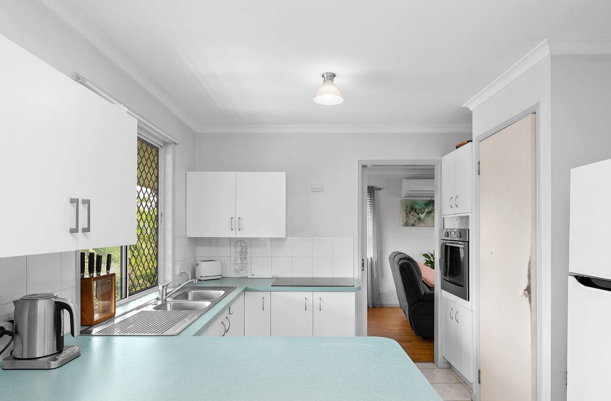 Kitchen before: laminate cabinets, teal benchtops and white wall tiles
