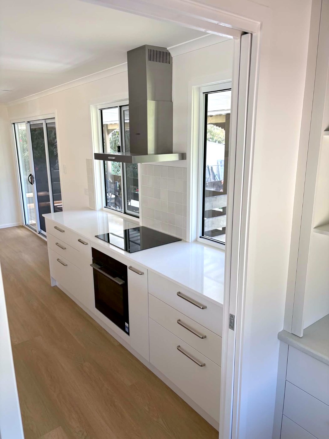 Kitchen after: cooktop run with stainless rangehood, sliding doors and timber-look floors