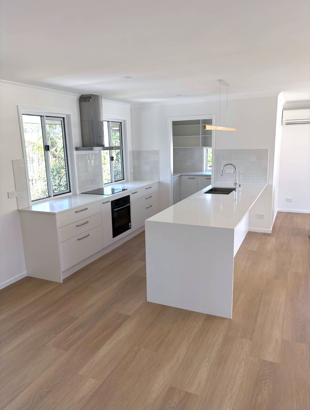 Kitchen after: white cabinetry, long waterfall stone island and timber-look floors