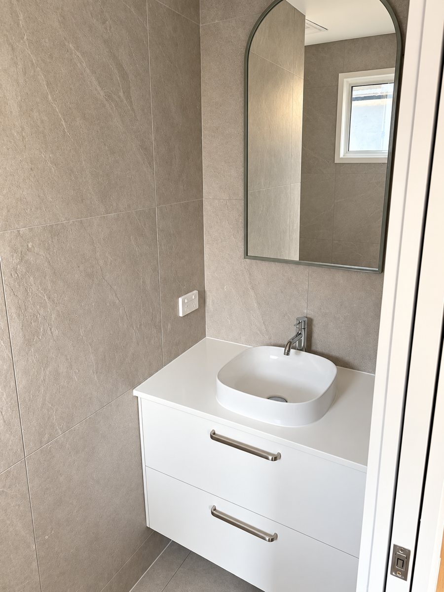 Powder room with wall-hung vanity, arched mirror and large stone-look tiles