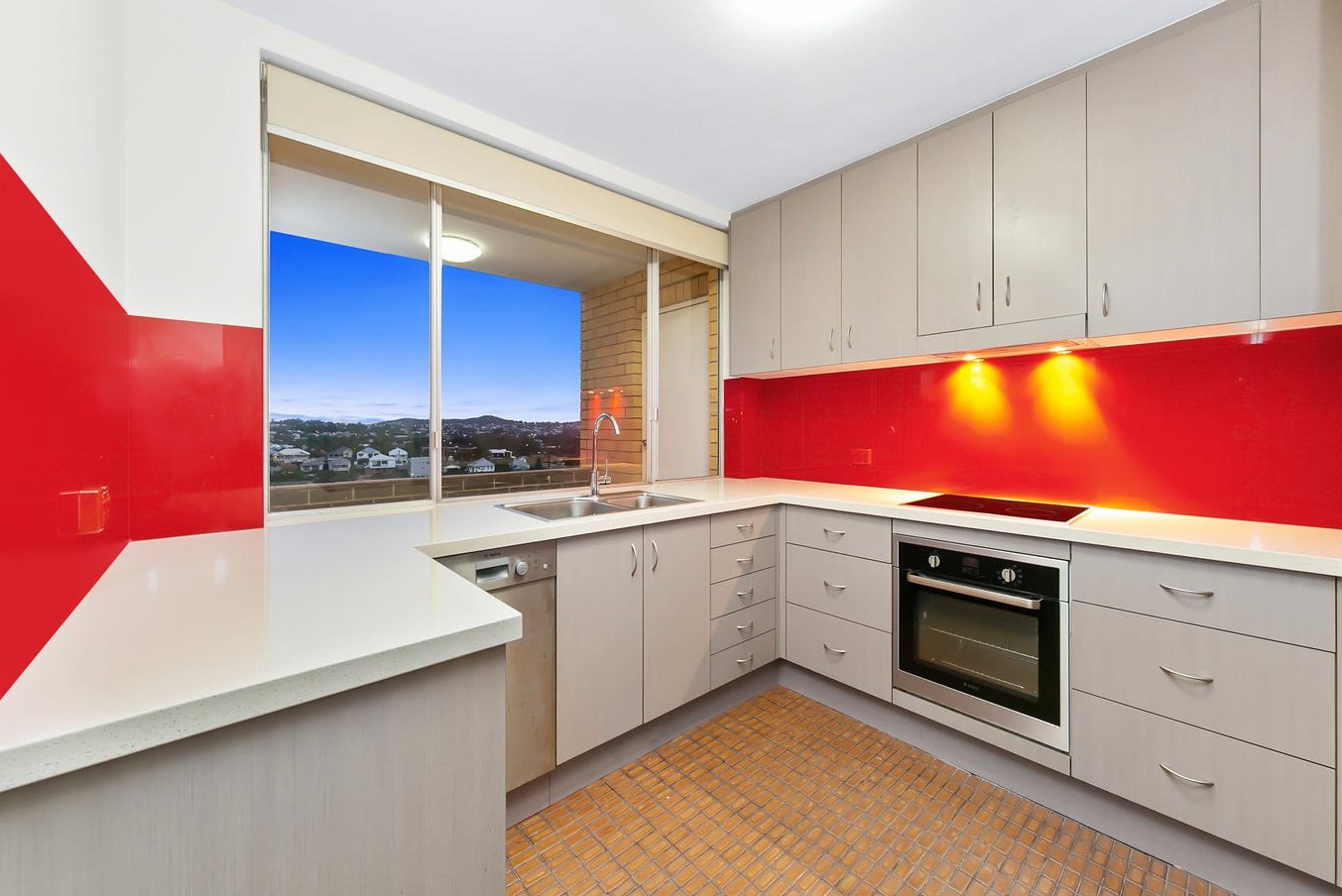 Kitchen before: grey laminate cabinets, red glass splashback and orange tiled floor