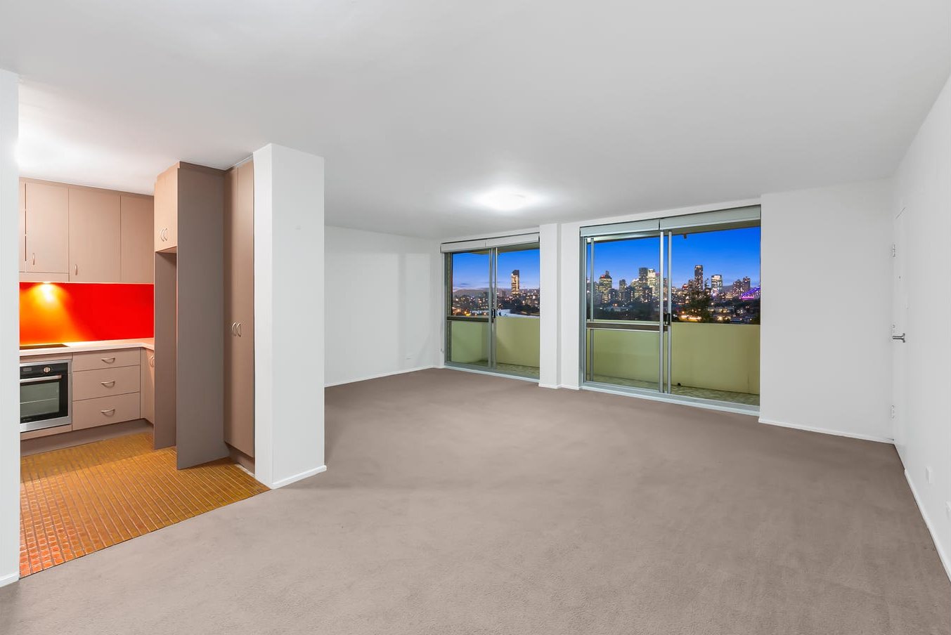 Living area before: beige carpet and a closed-in kitchen with red splashback